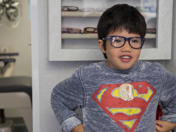 Pediatric patient with a superman shirt and glasses, standing in front of glasses case