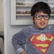 Pediatric patient with a superman shirt and glasses, standing in front of glasses case